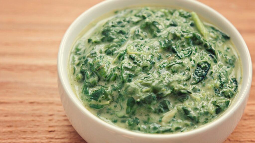 Close-up of creamy spinach in a white bowl, with visible chopped greens in a rich, thick sauce.