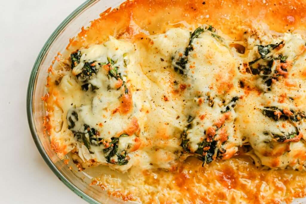 Cheesy baked chicken topped with spinach and melted cheese, browned and bubbly in a glass baking dish.