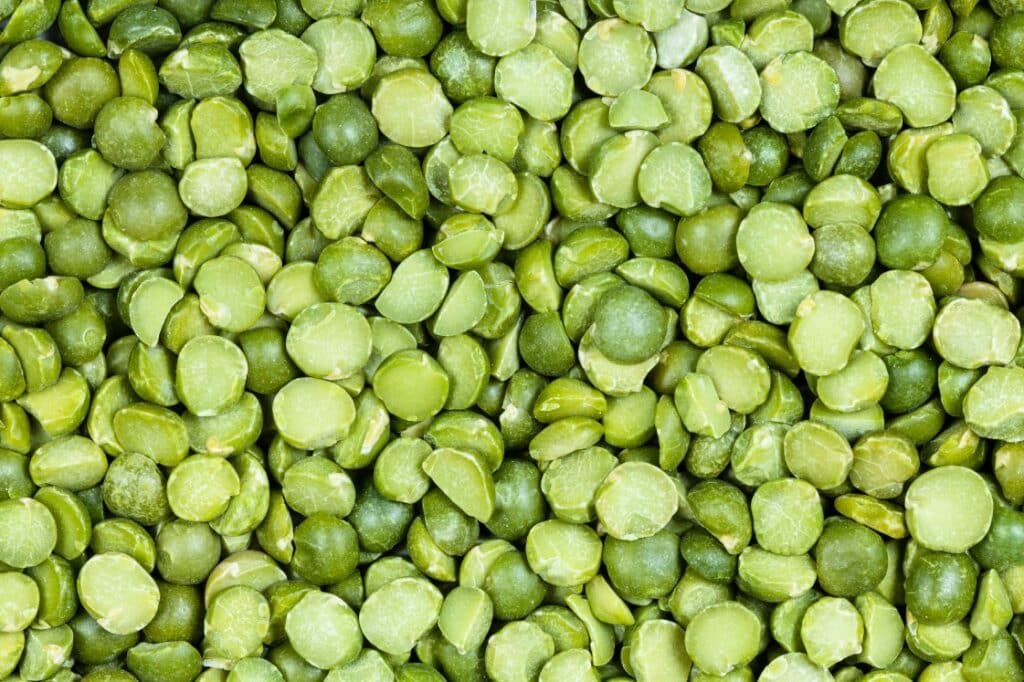 A close-up view of a pile of dried green split peas, showing their round, flat, and slightly rough texture.