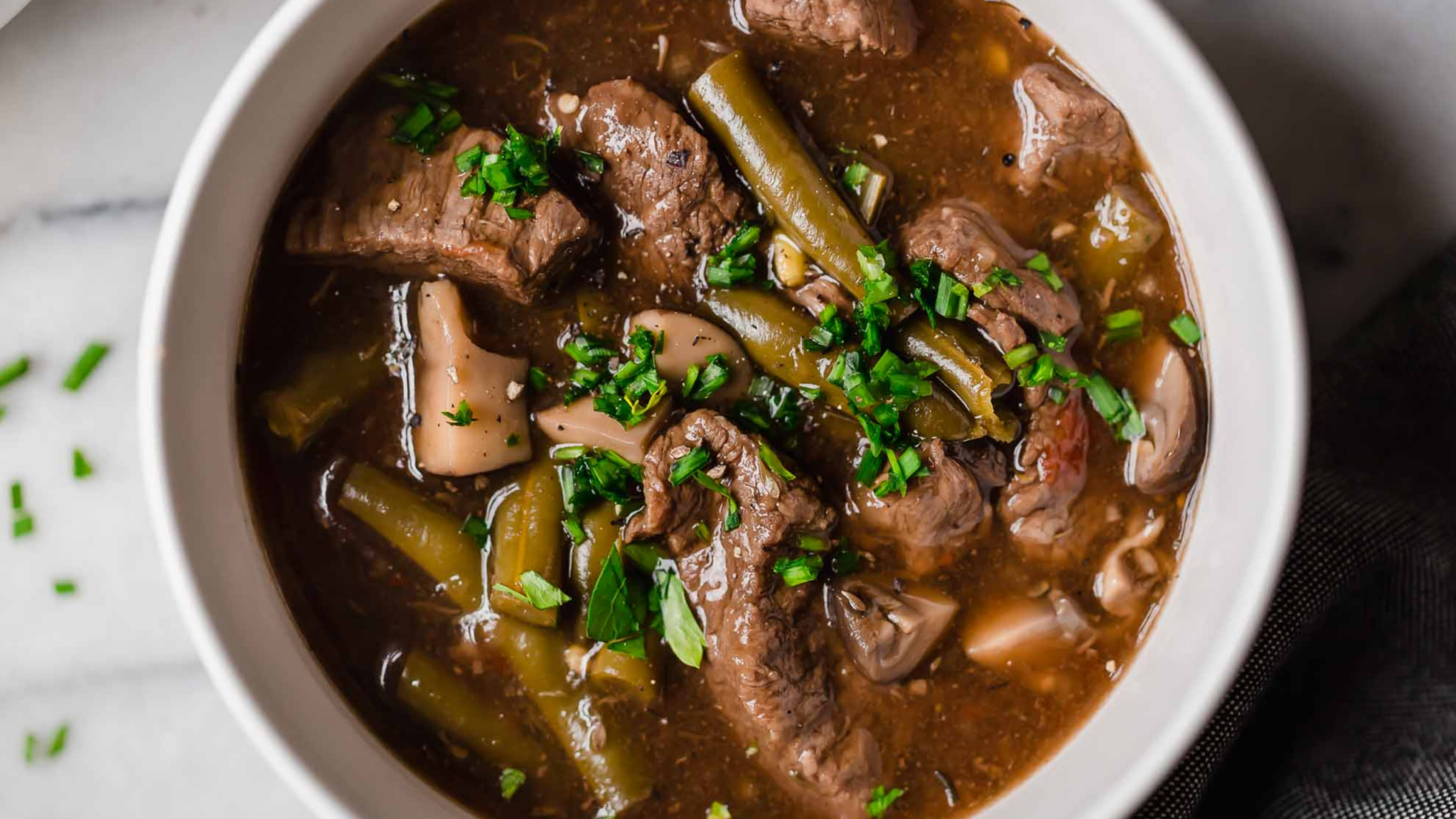 Instant Pot beef stew with green beans and mushrooms in a rich brown broth, garnished with fresh herbs.