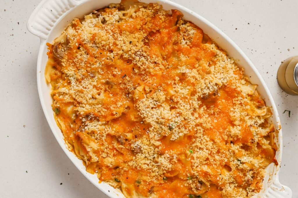 A baked tuna casserole dish filled with golden brown, cheesy noodles topped with crispy breadcrumbs, sitting on a light-colored surface.