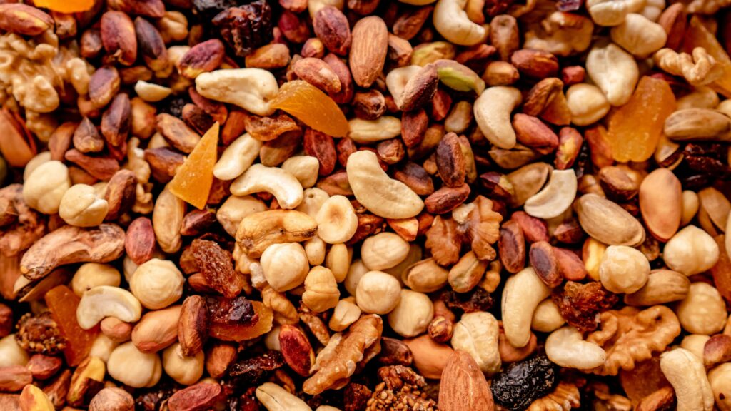 Close-up view of a colorful mix of roasted nuts, including cashews, almonds, pistachios, hazelnuts, and dried fruit pieces.
