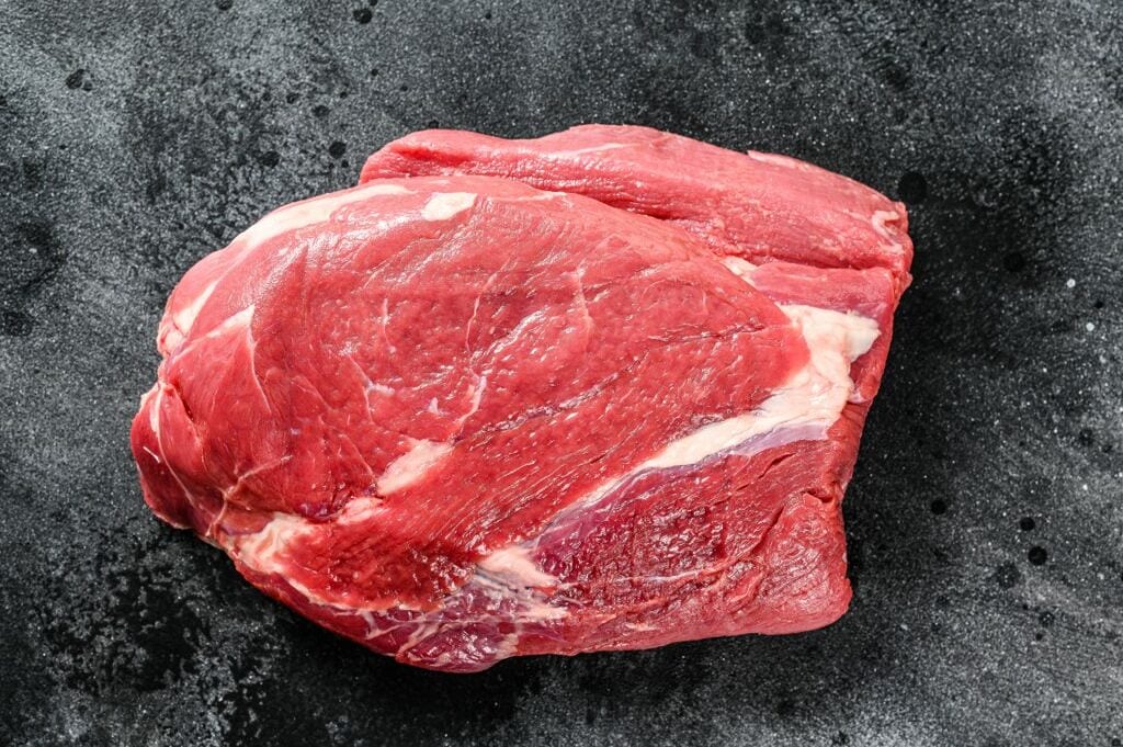 A raw beef chuck roast with visible marbling and fat, placed on a dark, textured surface.