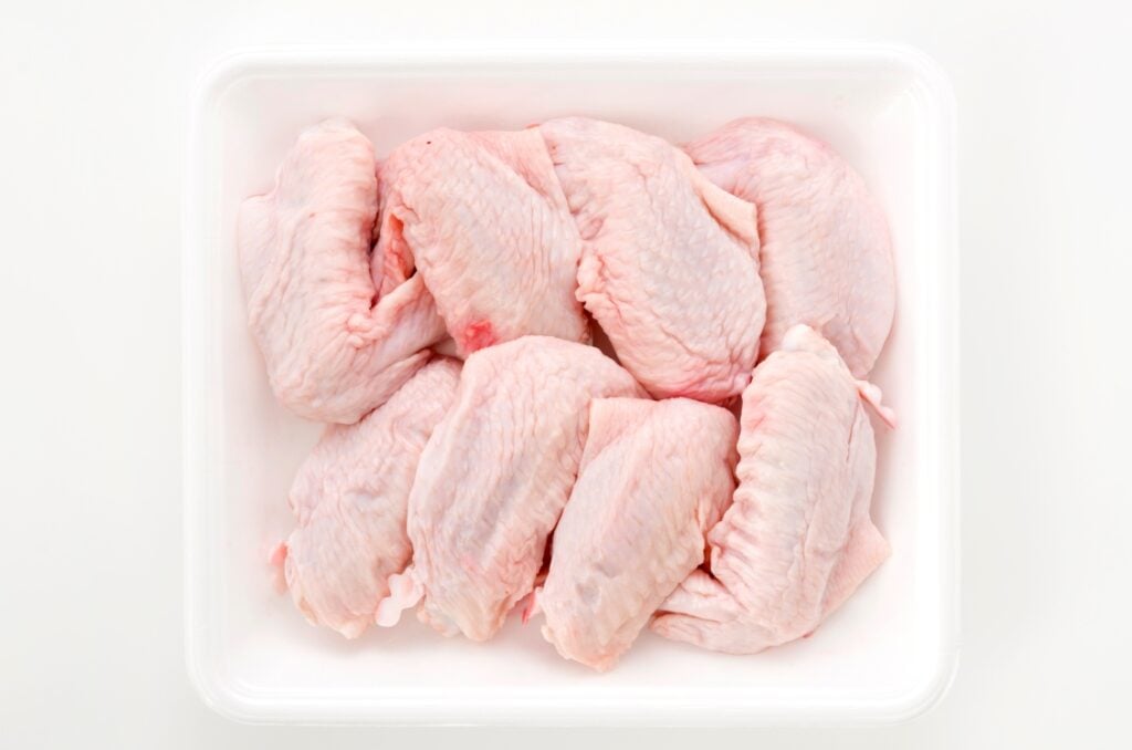 A white tray containing several raw chicken wings, neatly arranged and uncooked, on a plain white background.