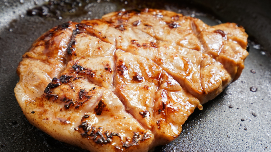 Golden-brown chicken breast fillet searing in a pan, scored with crosshatch marks and glistening with juices.