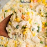 A wooden spoon scoops creamy chicken orzo pasta with corn, peas, carrots, and spinach from a pan. The dish looks rich and colorful. Text on the image reads: "Creamy Chicken Orzo Pasta.