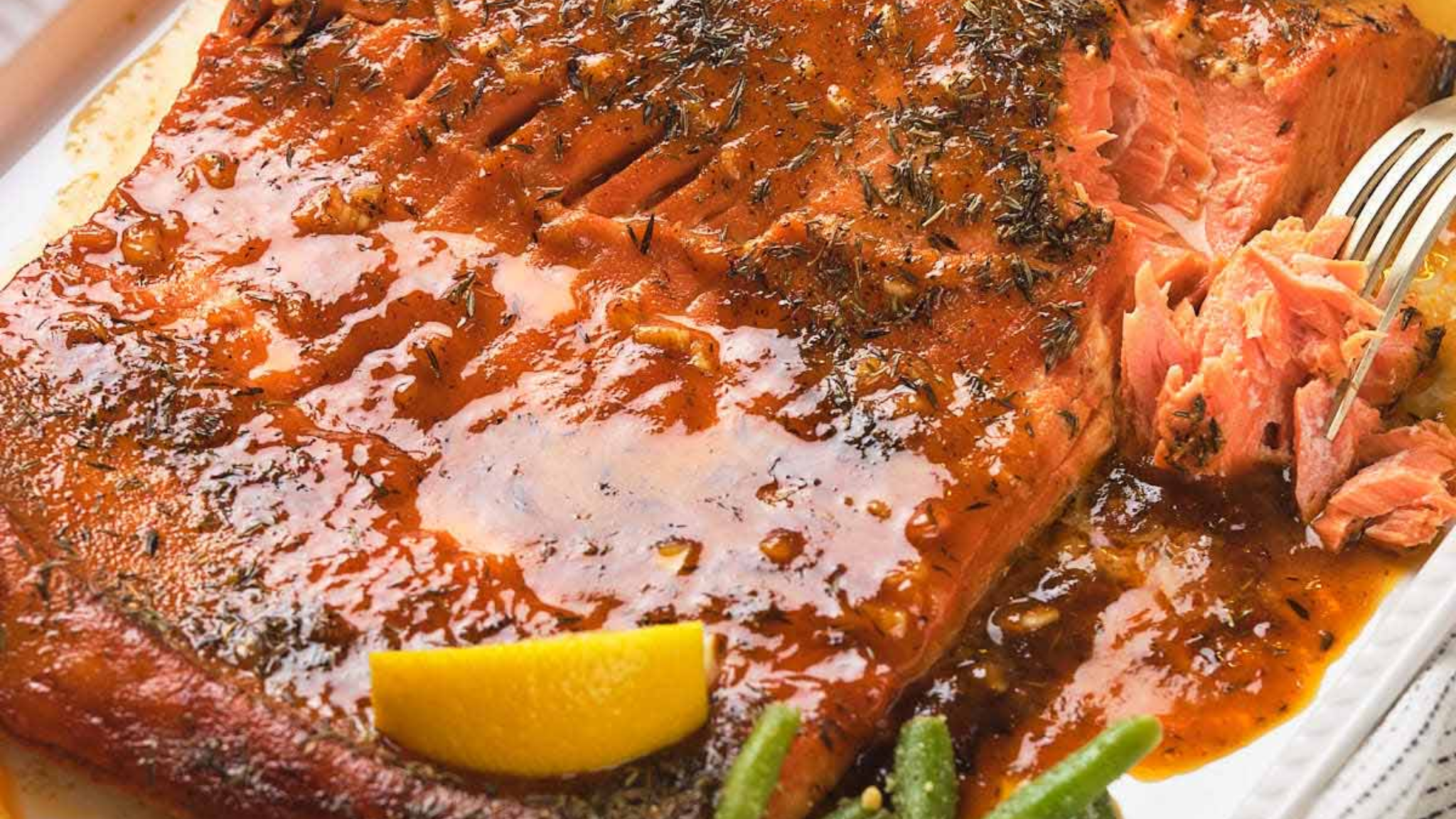 Honey mustard salmon with a glossy glaze, garnished with herbs and served with lemon wedges on a white plate.