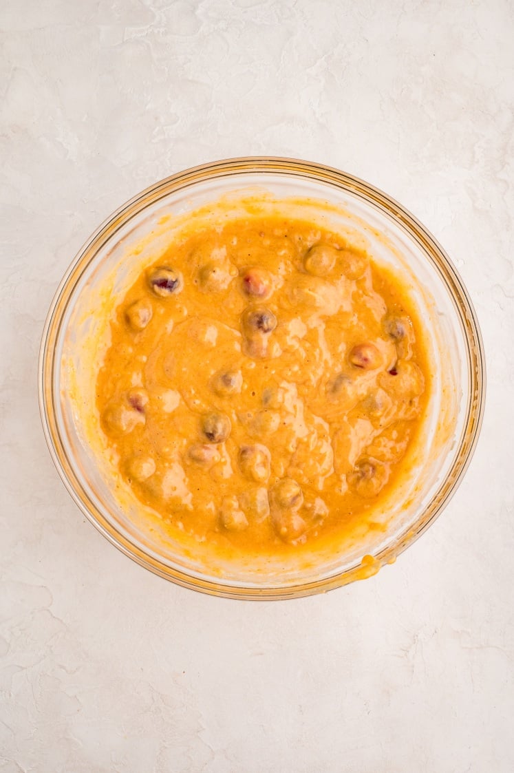 A glass mixing bowl containing a thick, orange batter with visible chocolate chips or chunks, placed on a light-colored, textured surface.
