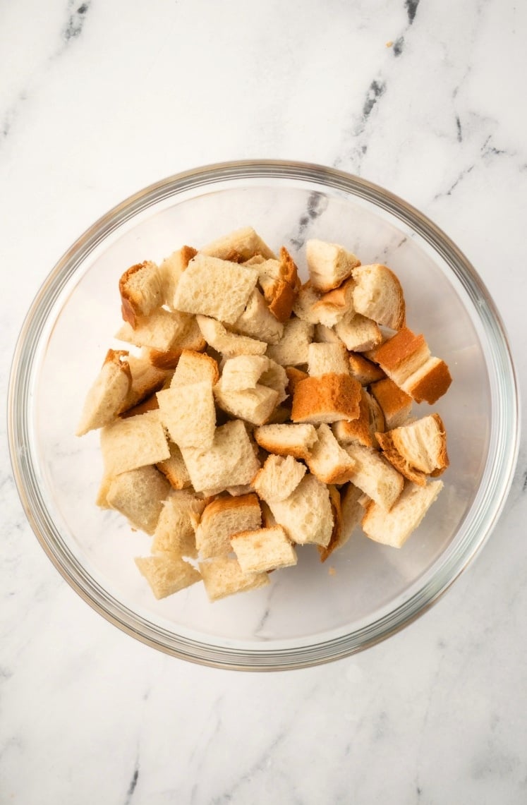 A glass bowl filled with cubed pieces of bread, perfect for making Air Fryer Croutons, sits on a white marble surface.