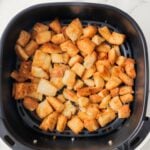 Air Fryer Croutons, golden brown and perfectly crispy, are evenly spread in a basket on a white marble surface.