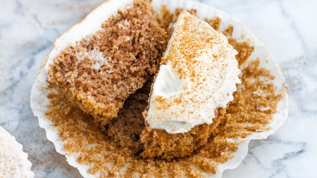 A cinnamon roll muffin sliced in half, revealing a moist, fluffy texture topped with cream cheese frosting and a dusting of cinnamon.