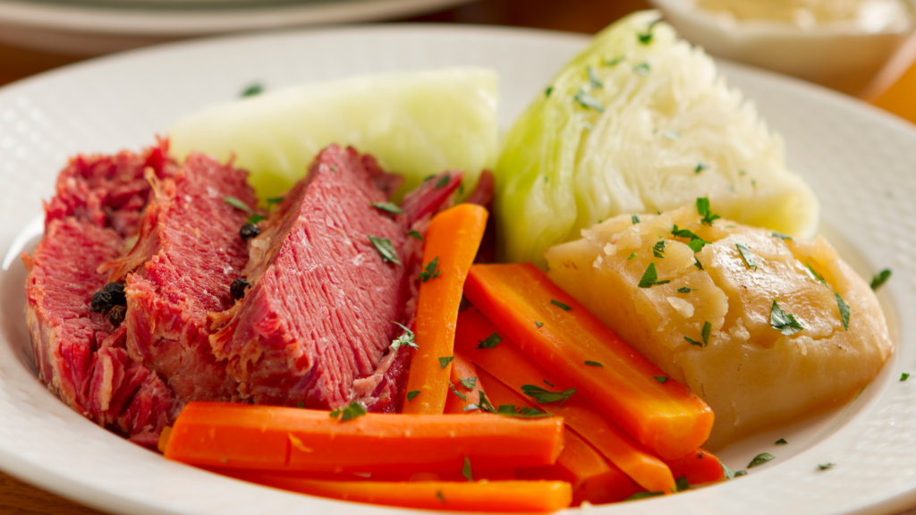 Corned beef slices served with boiled cabbage, carrots, and potatoes on a white plate.