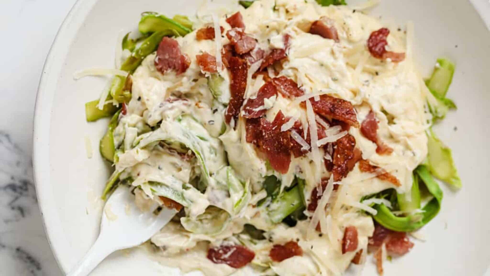 A bowl of creamy bacon asparagus pasta topped with crispy bacon bits and freshly grated parmesan. The pasta is coated in a rich, creamy sauce with pieces of tender asparagus, creating a comforting and delicious dish.