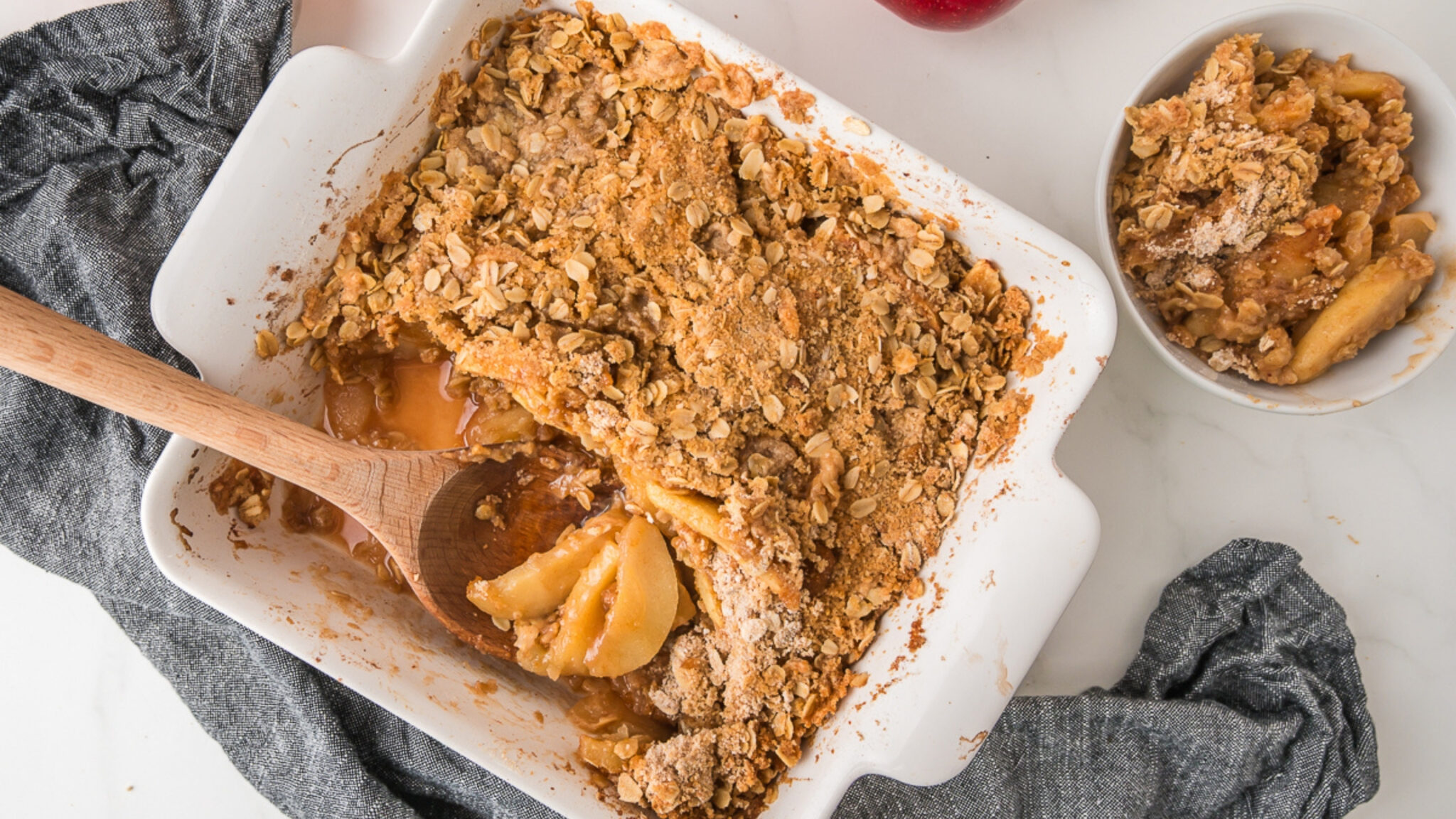 A bowl of apple crisp topped with a scoop of vanilla ice cream, featuring baked apple slices and crumbly oat topping.