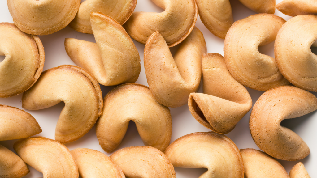 A pile of crisp golden-brown fortune cookies with folded edges and hollow centers.