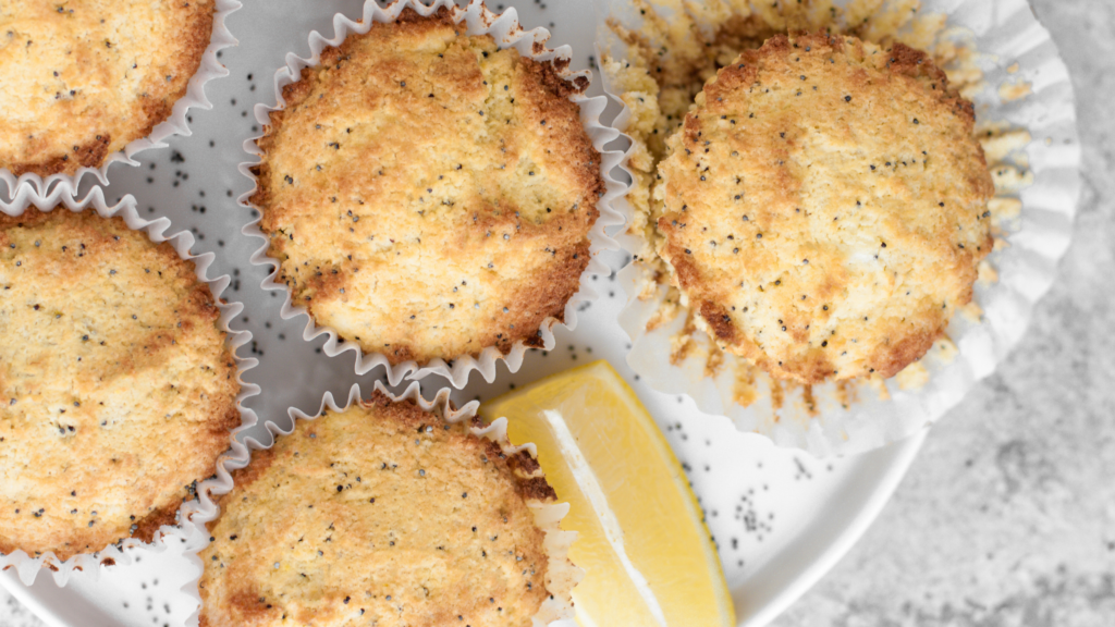 Lemon poppy seed muffins on a white plate, with lemon slices and scattered poppy seeds.