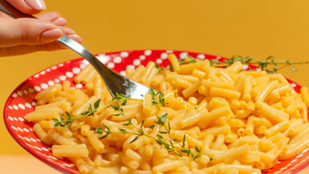 Fork scooping up creamy yellow macaroni and cheese, garnished with fresh thyme.