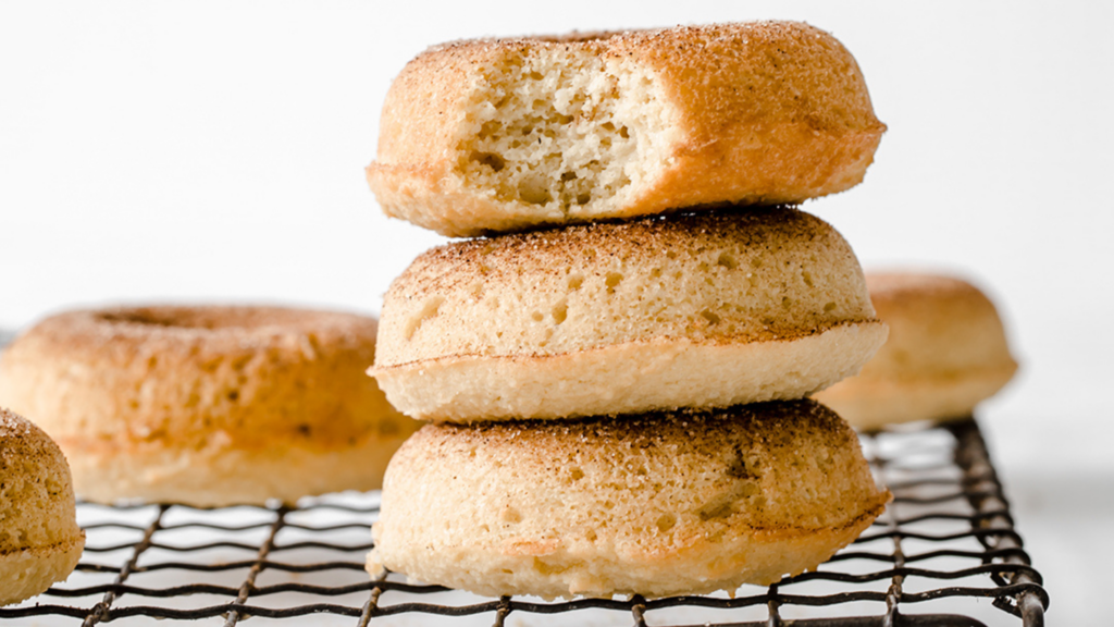 A stack of cinnamon sugar–coated keto donuts, with one donut showing a bite taken out.