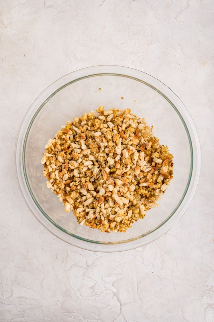 A clear glass bowl filled with a mixture of crumbled bread stuffing sits on a light, textured surface.