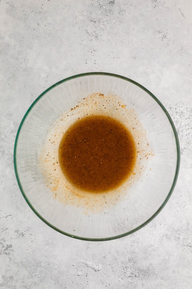 Glass bowl filled with blended marinade made from olive oil, garlic, spices, and seasonings.