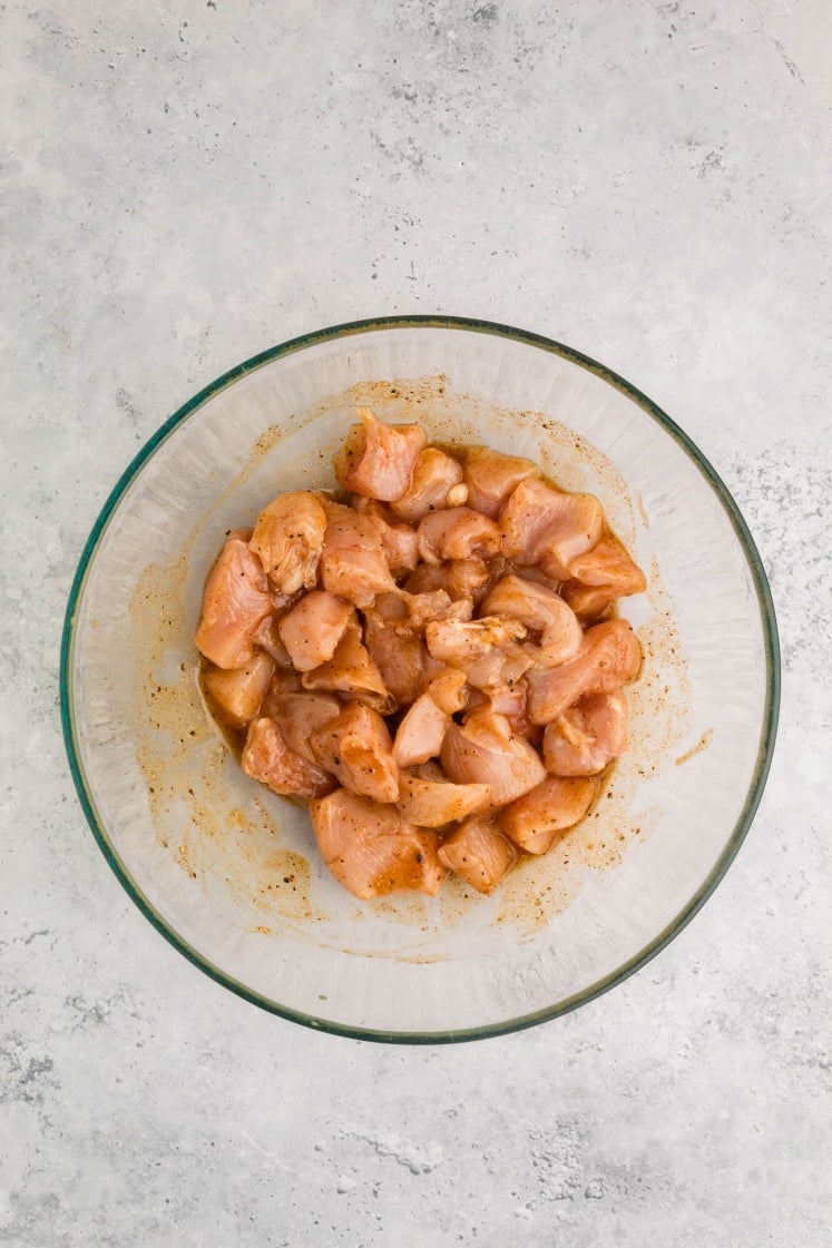 Glass bowl filled with blended marinade made from olive oil, garlic, spices, and seasonings for air fryer chicken skewers, sitting on a light gray countertop.