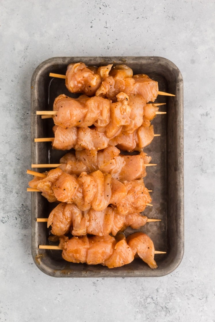Raw marinated chicken pieces threaded onto wooden skewers and arranged in a metal baking tray, ready to be cooked.