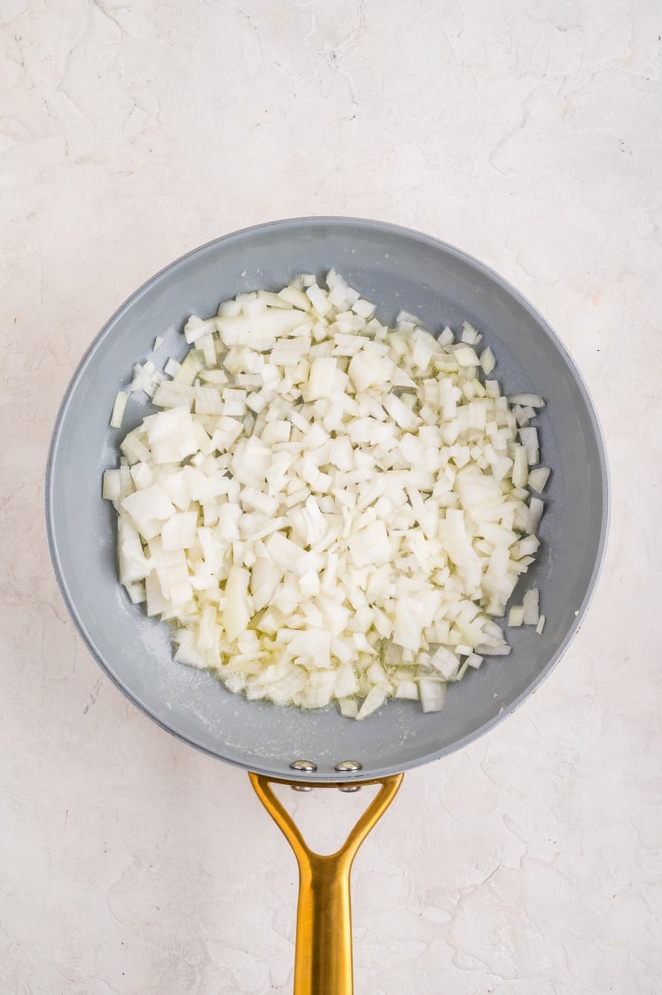 Skillet with diced yellow onions sautéing in butter for topping.