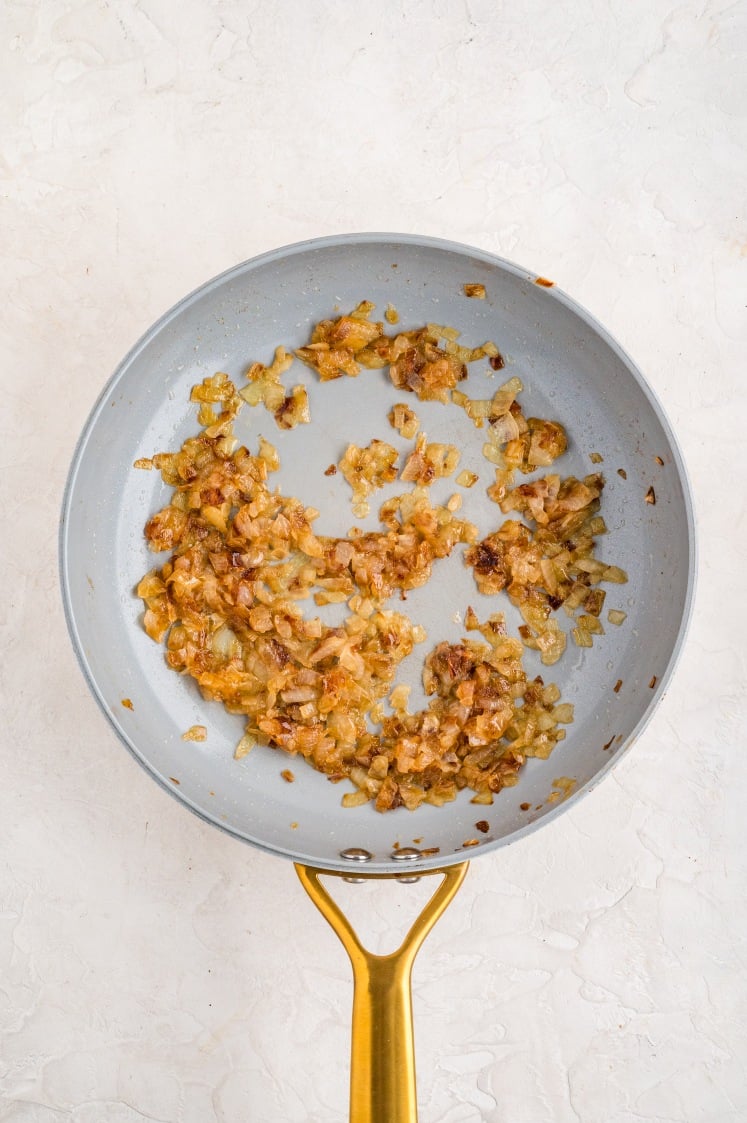 Caramelized diced onions cooking in a skillet with butter and brown sugar, turning golden and soft.