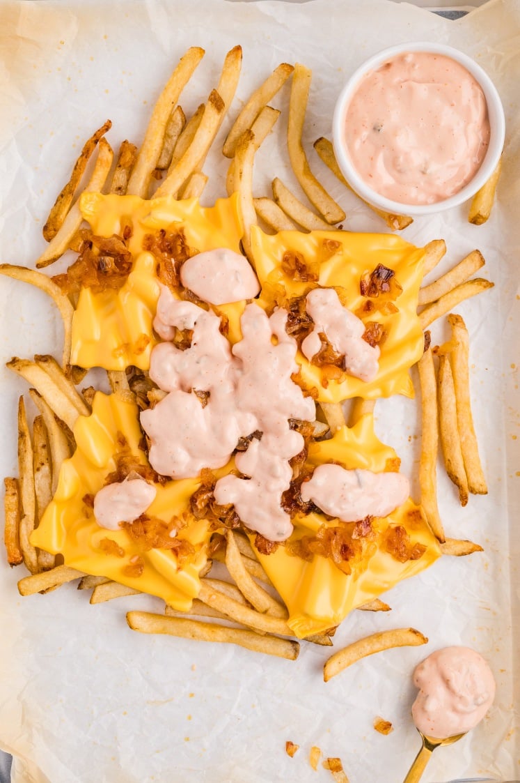 Animal-style fries topped with melted American cheese, caramelized onions, and creamy sauce served on a sheet pan with a side of dipping sauce.