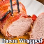 A crispy, glazed bacon wrapped pork tenderloin is being cut with a sharp knife and fork, with juices pooling on a white scalloped platter.