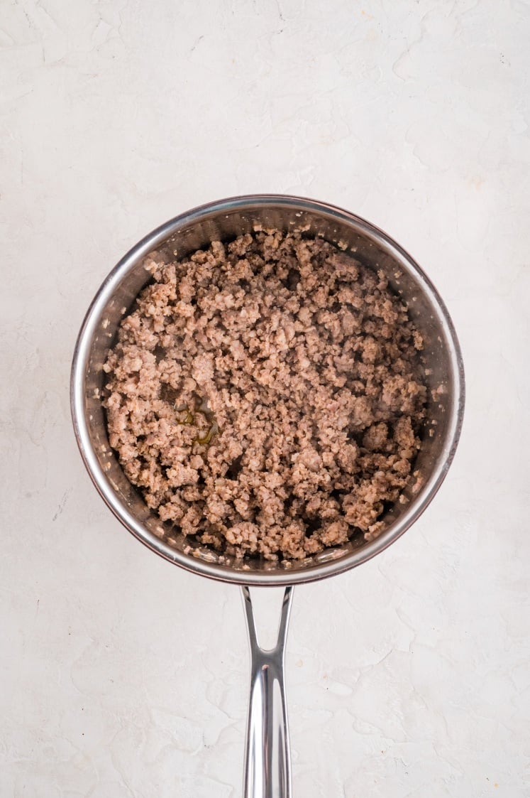 Cooked ground sausage in a stainless-steel skillet, with a light layer of steam rising from the meat against a neutral background.