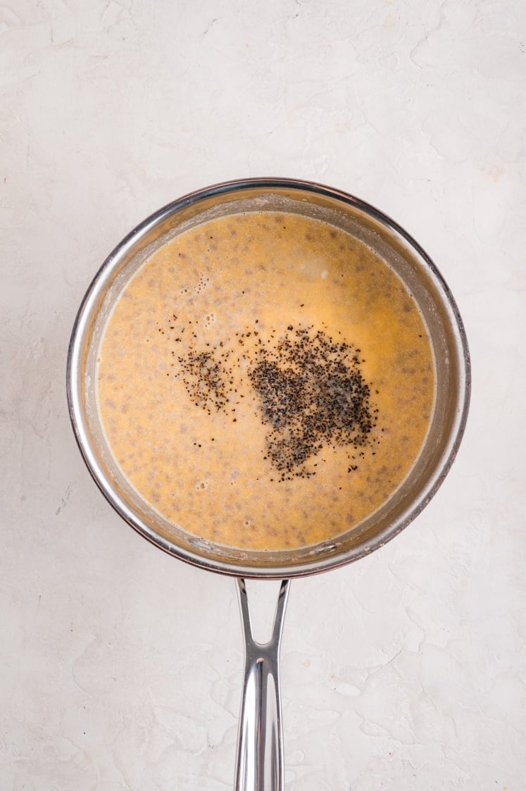 Milk, eggs, and black pepper whisked together in a mixing bowl to make the egg mixture for biscuits and gravy casserole.