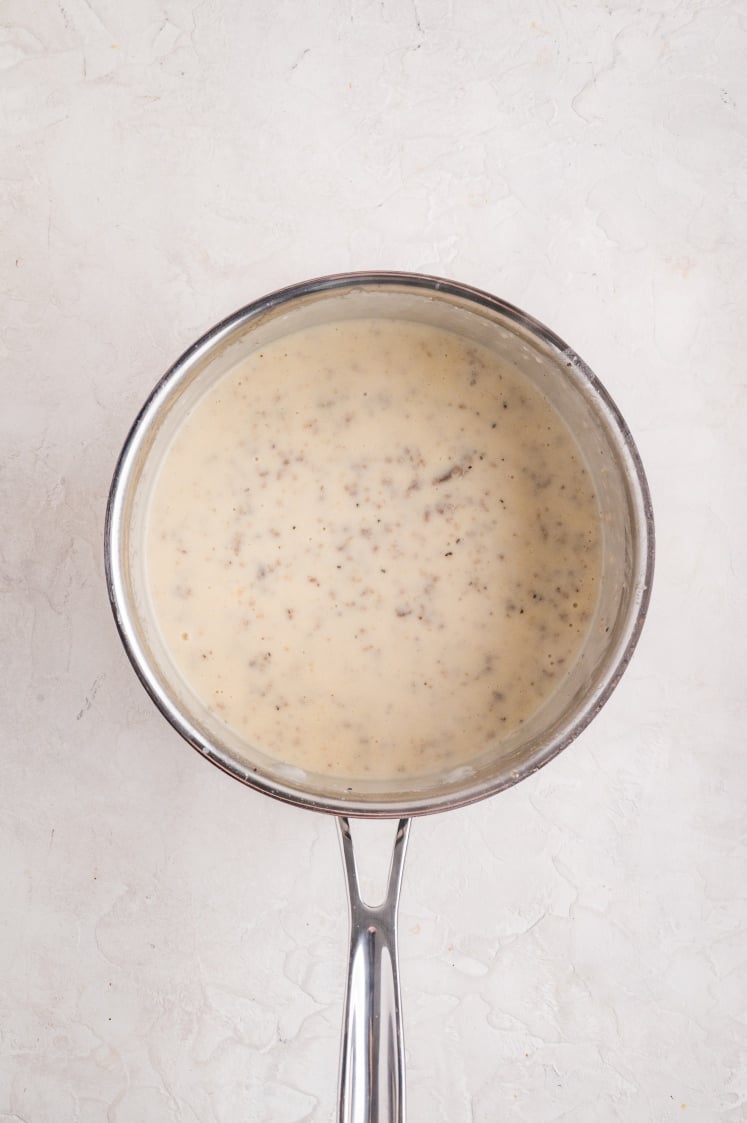 Creamy sausage gravy simmering in a saucepan, thickened and ready for the biscuits and gravy casserole.