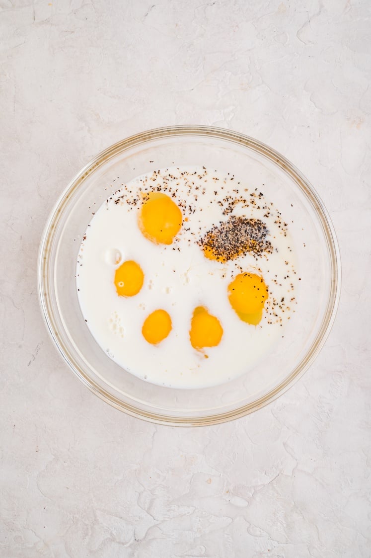 Eggs, milk, salt, and pepper sitting together in a glass bowl before being whisked for the breakfast casserole.