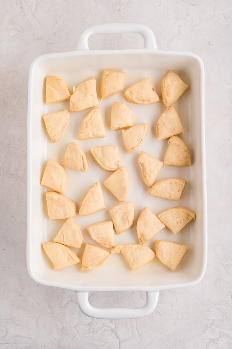 Unbaked biscuit pieces arranged evenly in a white casserole dish, ready for layering.