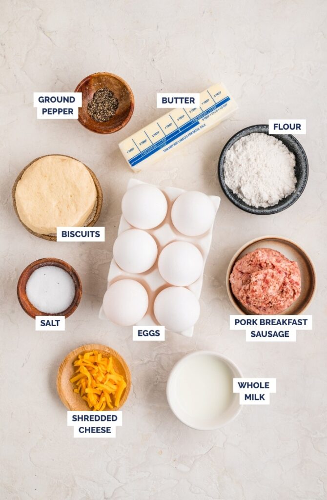 Ingredients for biscuits and gravy casserole including biscuits, eggs, sausage, milk, cheese, butter, flour, salt, and pepper.