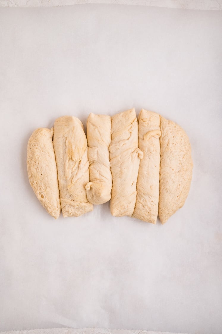 A portion of risen dough cut into six even sections and arranged on parchment paper, ready to be coated for cinnamon pull-apart bread.