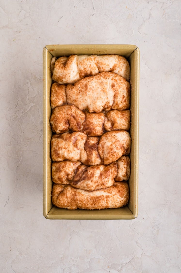 A loaf pan filled with unbaked cinnamon pull apart bread dough pieces, arranged closely together and sprinkled with cinnamon sugar for a classic treat.