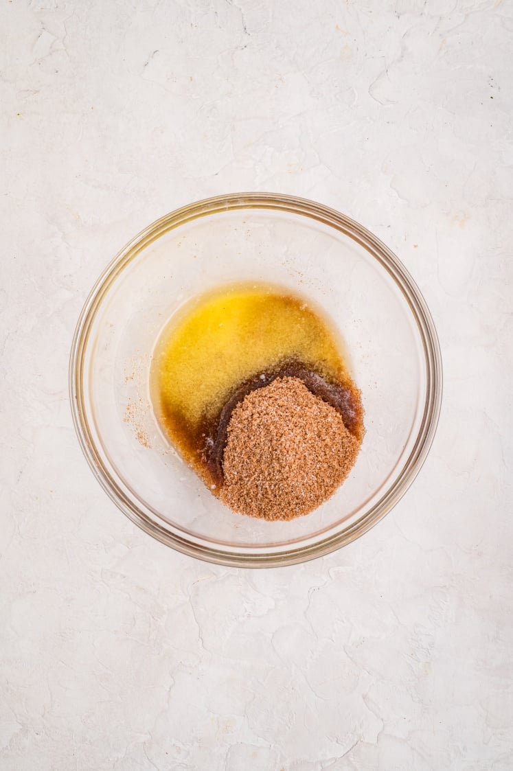 A glass bowl containing melted butter and a mound of cinnamon-sugar mixture before being stirred together for the pull-apart bread filling.