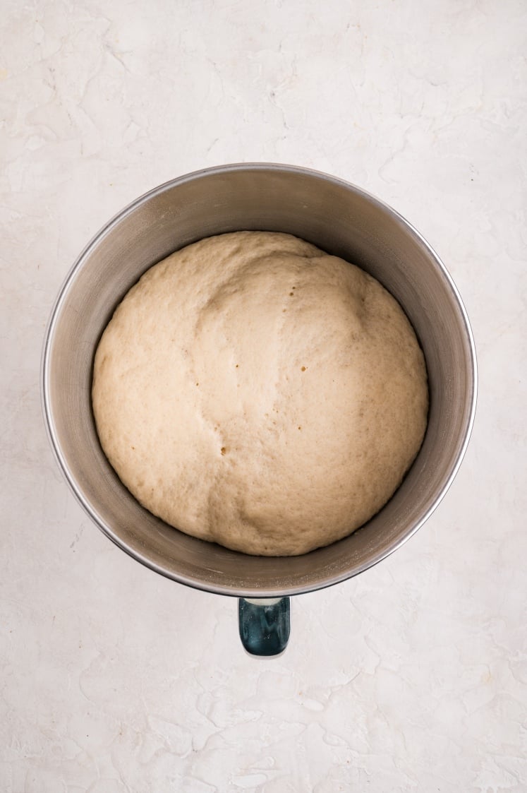 A stainless steel mixing bowl filled with risen dough that has doubled in size, showing its smooth, airy texture after proofing.