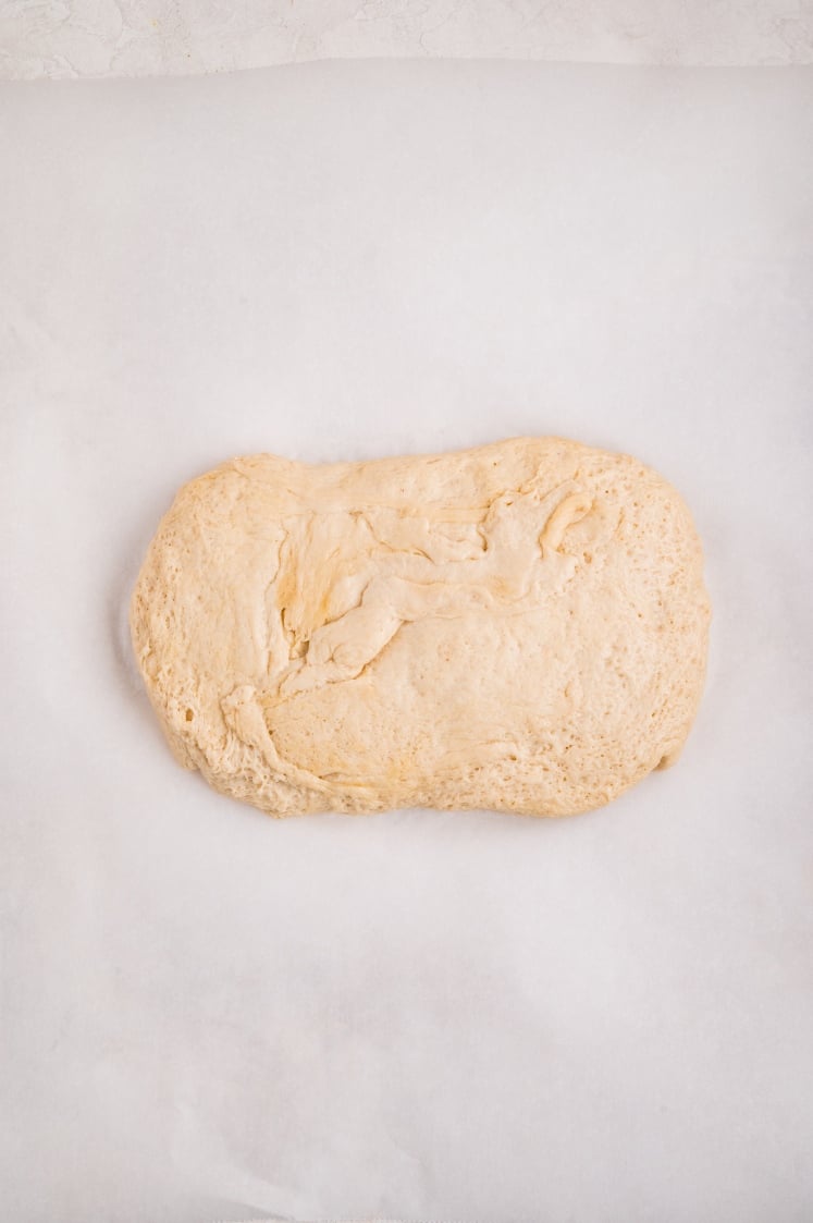A piece of risen dough turned out onto a sheet of parchment paper, ready to be shaped and rolled for cinnamon pull-apart bread.