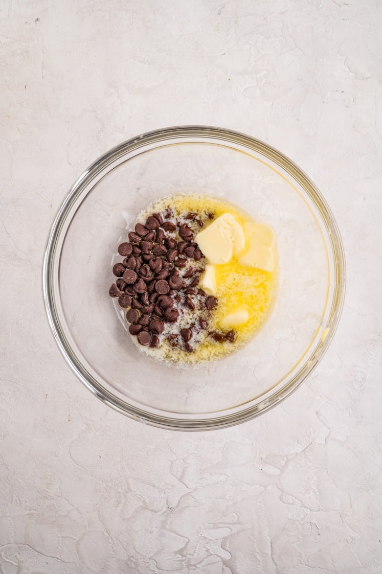 A glass mixing bowl filled with melted butter and chocolate chips, beginning to melt together for the brownie batter.