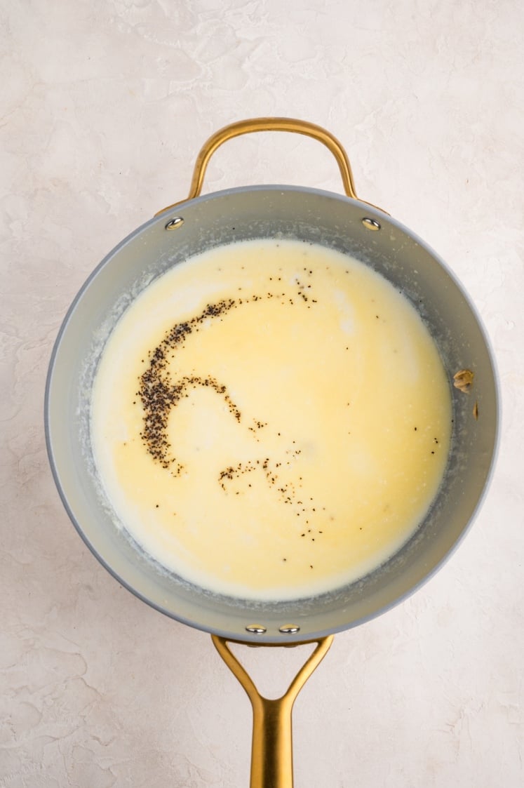 A saucepan with melted butter and cracked black pepper sprinkled on top, viewed from above, on a light-colored surface.