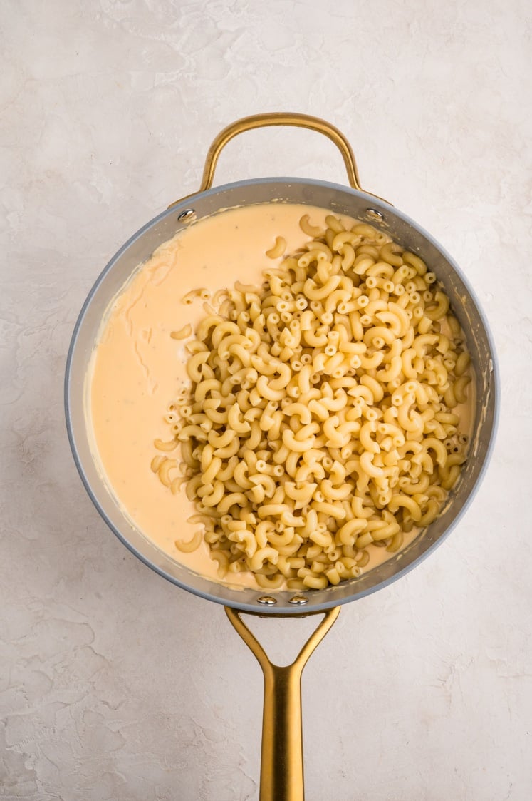 A pot with cooked elbow macaroni partially mixed into creamy cheese sauce, sitting on a light-colored surface.