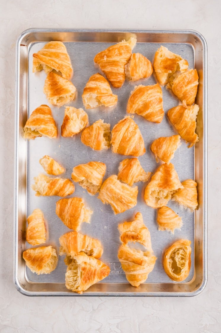 Tray of torn croissants arranged on a baking sheet, ready to be used for a breakfast bake.