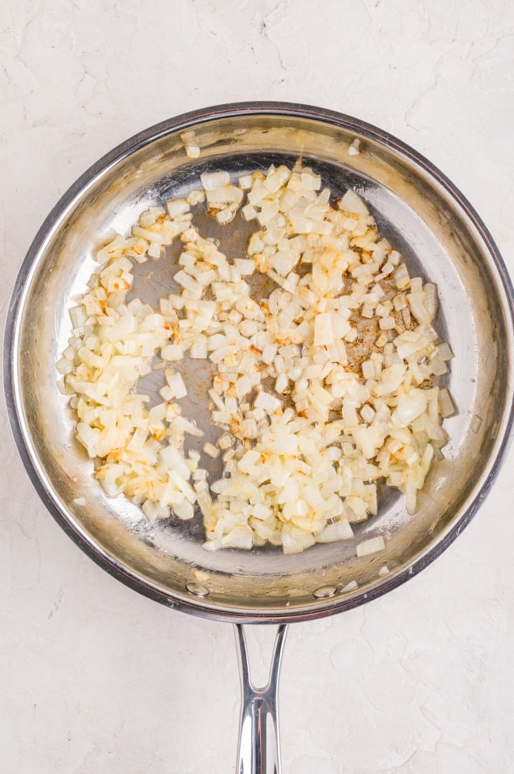 Chopped yellow onions in a skillet before sautéing for the ham and cheese croissant breakfast bake.