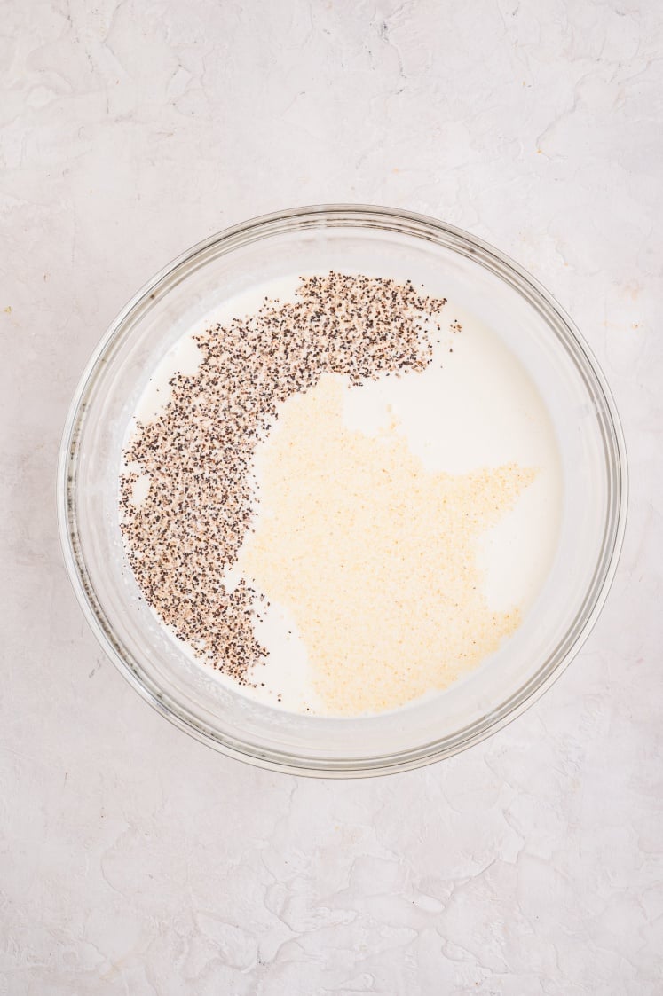A glass mixing bowl filled with milk, garlic powder, and black pepper before being whisked together for a Ham and Cheese Croissant Breakfast Bake.