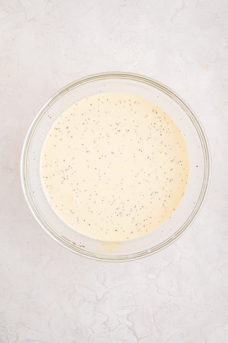 Smooth egg and cream mixture speckled with black pepper and seasonings in a glass bowl, ready to pour over the ham and cheese croissant bake.