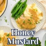 A plated serving of honey mustard pork chops with mashed potatoes and green beans, surrounded by fresh parsley, honey, and serving utensils on a bright kitchen surface.