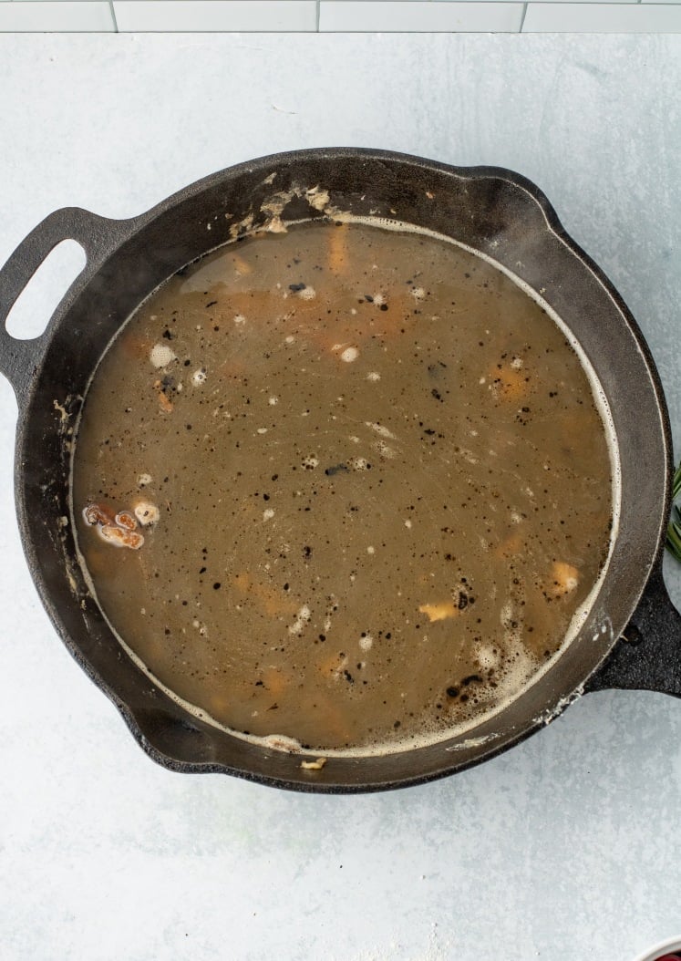 Cast-iron skillet filled with simmering broth and seasonings, creating a flavorful base.
